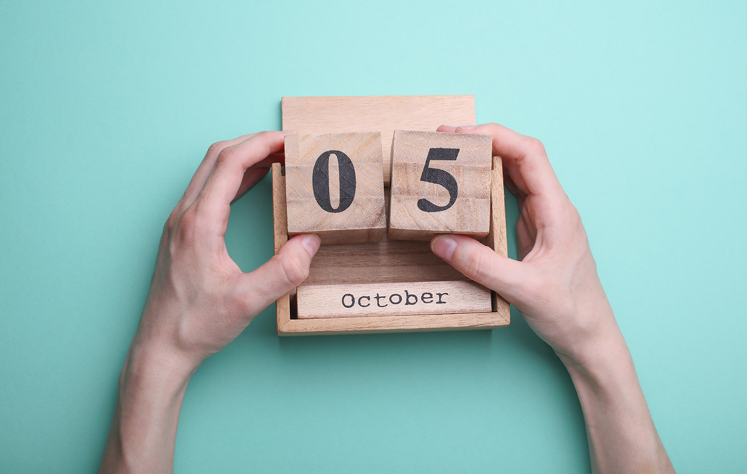 Hand holding wooden block calendar with date october 05 on mint green background