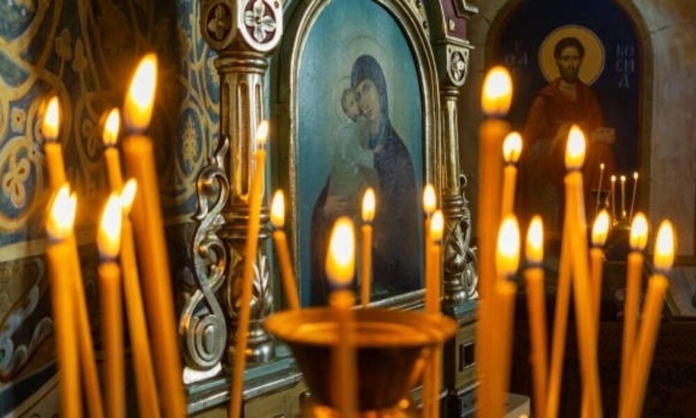 Blurred wax burning candles in an orthodox church on the icon background.