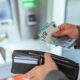 A,Person,Accessing,An,Atm,And,Holding,Euro,Currency,Notes